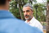 an older man listens to another man wearing a blue shirt while they walk outdoors